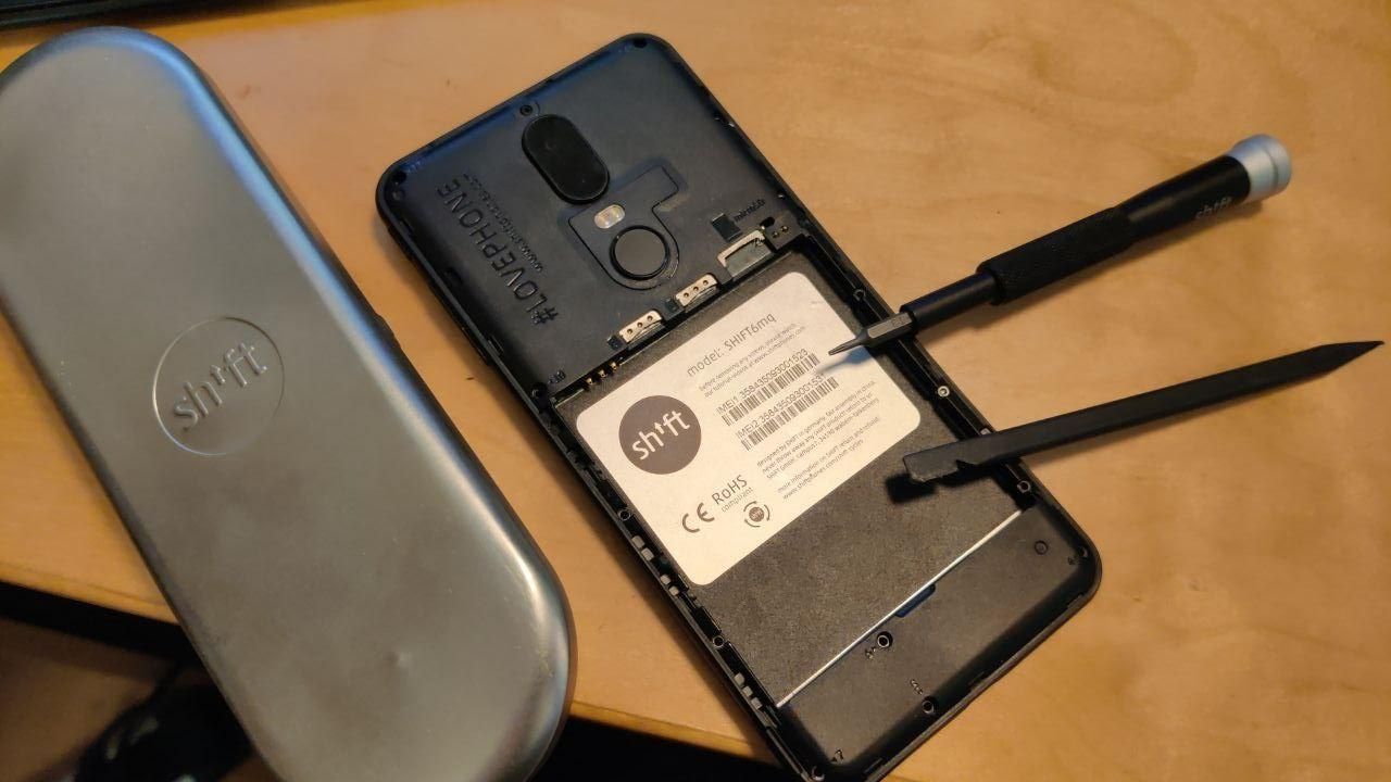 A picture of the back of a SHIFT6mq with the back cover and battery removed, a pry tool and ifixit screwdriver are resting 
